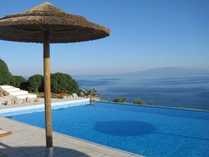 A swimming pool with a thatched umbrella, surrounded by a landscaped area with steps and plants, overlooking a body of water. - Mar Y Sol (Mykonos)