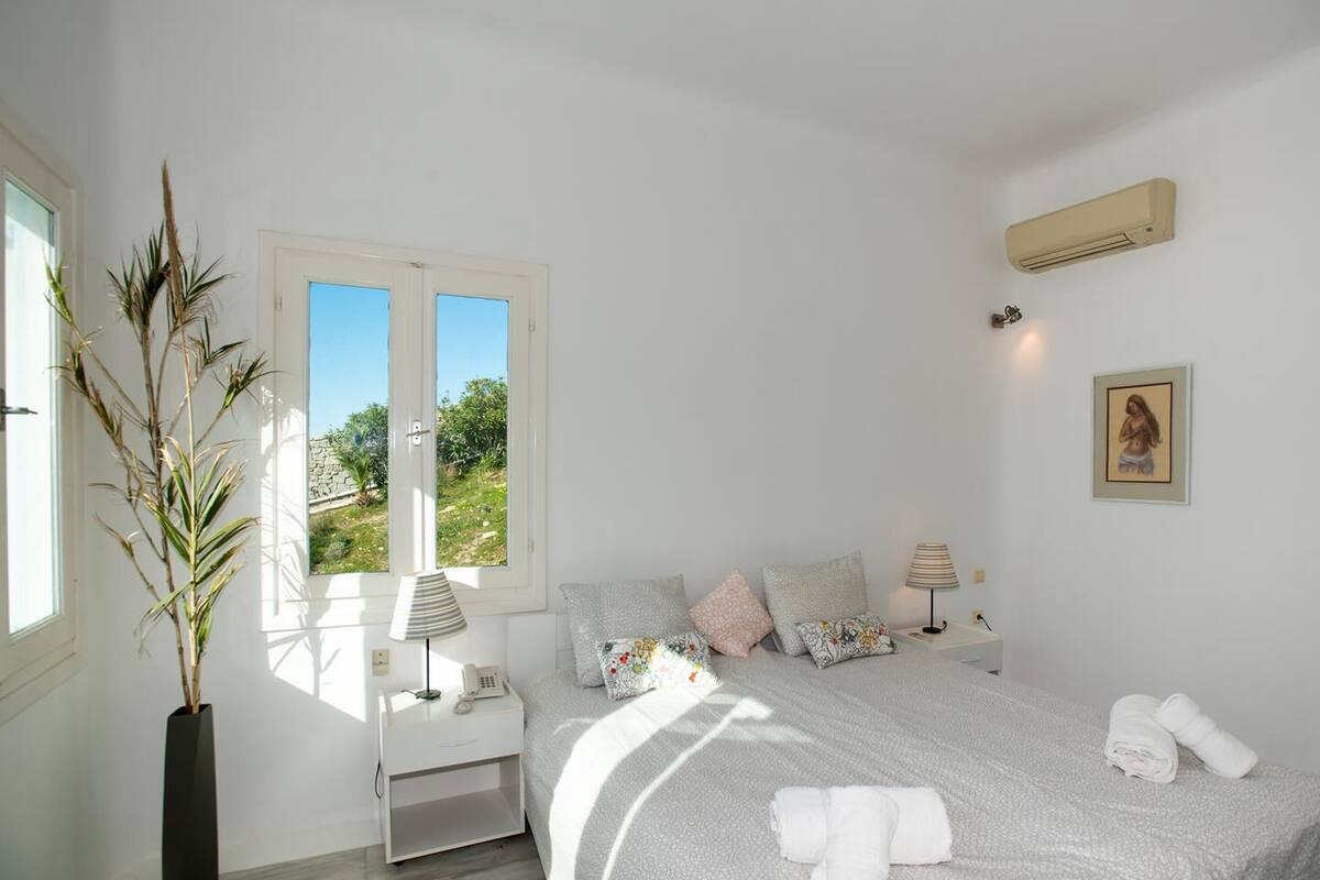 A bedroom with a bed, bedside tables, a lamp, a painting, and a view of greenery outside.