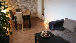 A dining area with a wooden table and chairs, a black coffee table with decorative items, a brown sofa, and a brick-patterned wall. - Robs Ferienwohnung (Dresden)