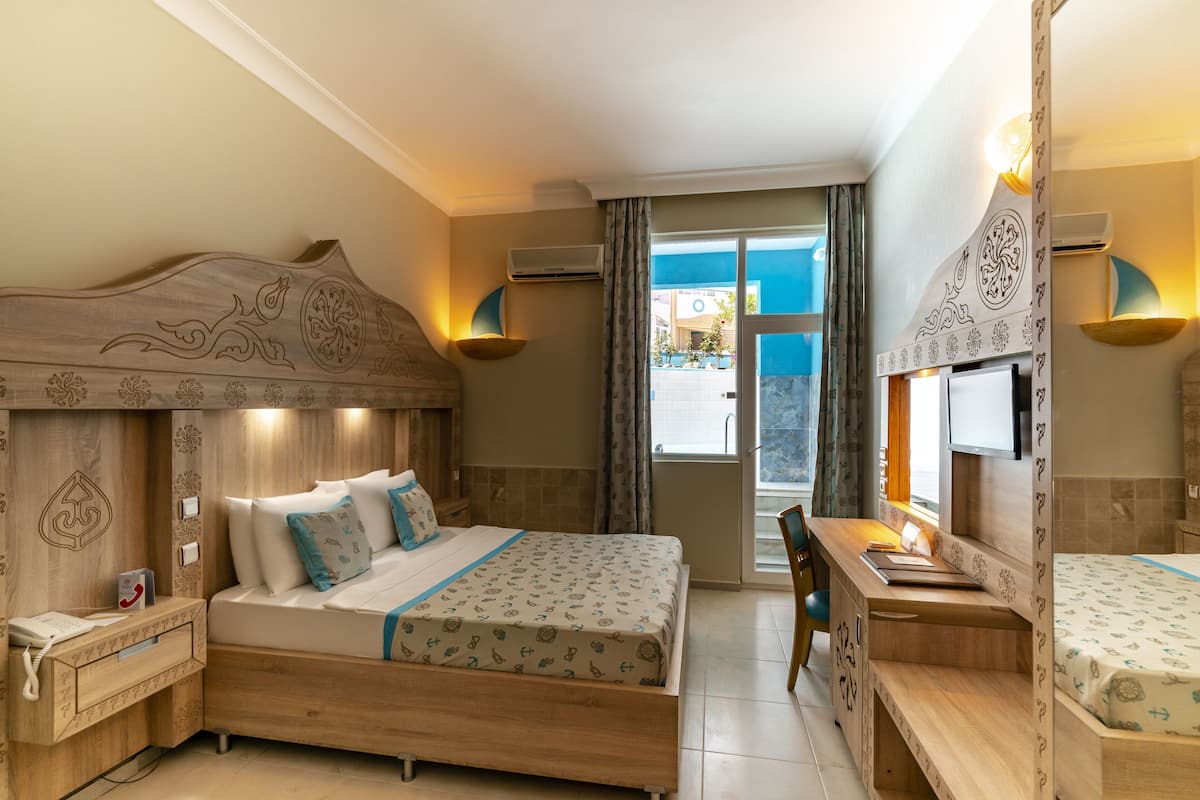 A hotel room with a wooden bed, a desk, a chair, a telephone, and a window with curtains.