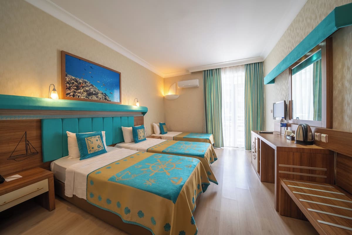 A hotel room with three beds, a wooden desk, a television, and a painting of a coral reef.
