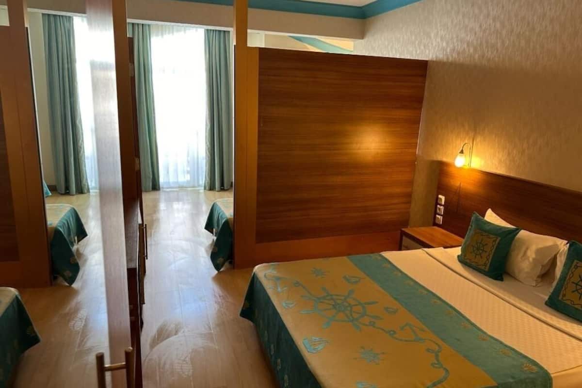 A hotel room with a large bed, a wooden headboard, a nightstand, and a wall-mounted lamp.