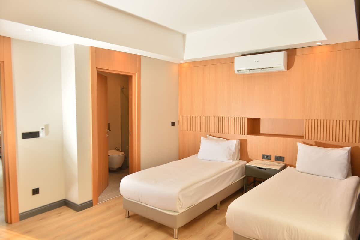 A hotel room with two beds, a wooden headboard, a small bedside table, and an air conditioning unit.