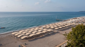 A beach with rows of sun umbrellas and lounge chairs, a pier extending into the sea, and a clear sky. - Miarosa Kemer Beach (Kemer)