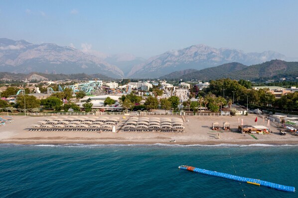 An aerial view of a coastal area with a beach, a water slide, and mountains in the background. - Miarosa Kemer Beach (Kemer)