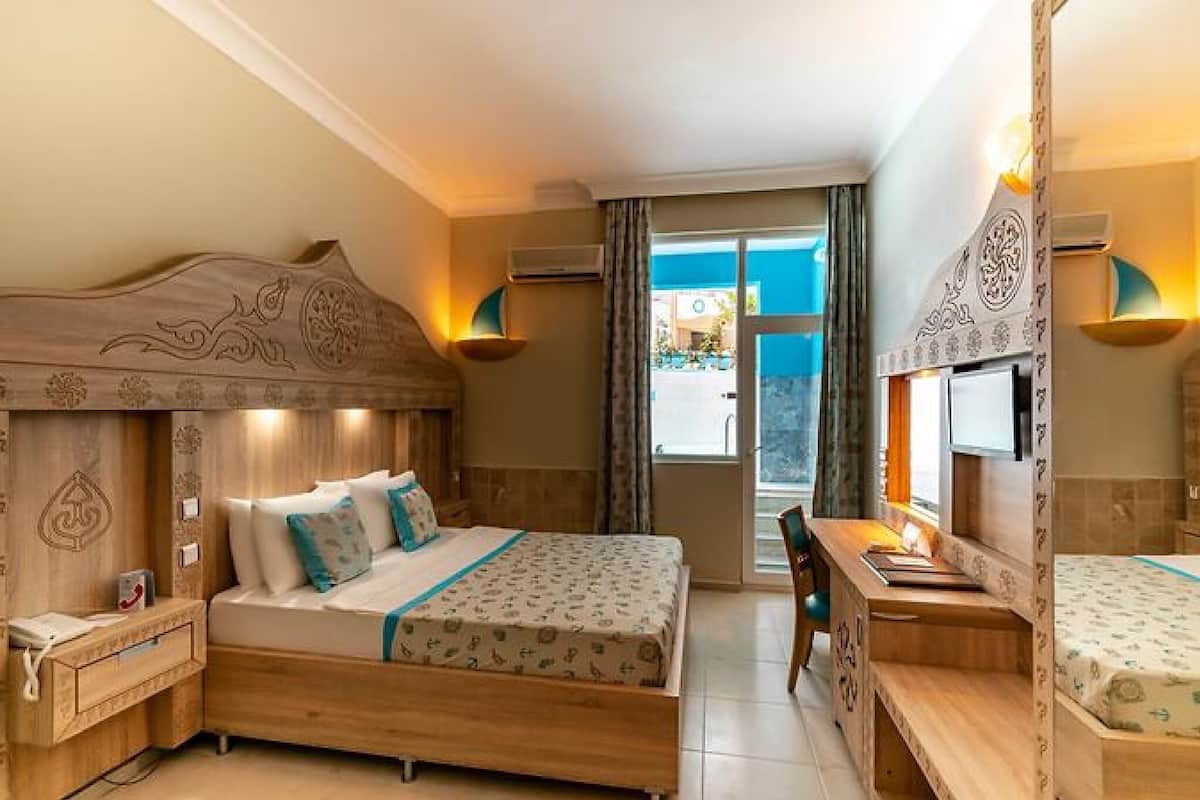 A hotel room with a large bed, a desk, and a chair. There is a window with a view of the outside.