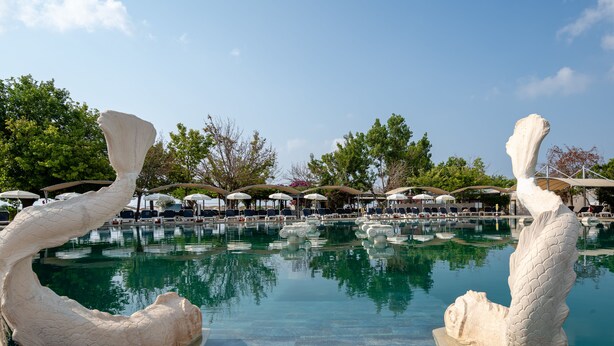 A pool area with two large white sculptures, lounge chairs, umbrellas, and a clear blue sky. - Miarosa Kemer Beach (Kemer)