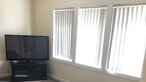 A living room with a flat-screen TV on a stand, a brown leather sofa, and a carpeted floor. - Entire House 3 bedrooms, 5 minute walk to town centre and 1 minute to beach (Strahan)