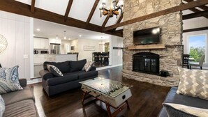 A spacious living room with a stone fireplace, a sofa, and a foosball table. - Cabin on the Hill - North Nashville Stunner! (Hendersonville)