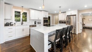 A modern kitchen with white cabinets, stainless steel appliances, and a large island with bar stools. - Cabin on the Hill - North Nashville Stunner! (Hendersonville)