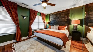 A bedroom with a bed, a ceiling fan, a nightstand with a lamp, and a wall with a wooden texture. - Walk to Broadway - Heart of downtown (Nashville)