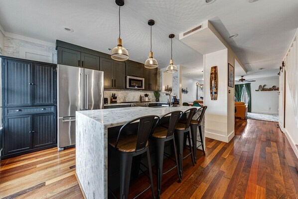 A modern kitchen with a marble island, dark cabinets, stainless steel appliances, and a hardwood floor.