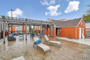 An outdoor patio area with lounge chairs, a pergola, and a brick building.