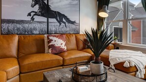 A living room with a brown leather sofa, a coffee table with a plant, and a window with curtains. - Walk to Broadway - Heart of downtown (Nashville)