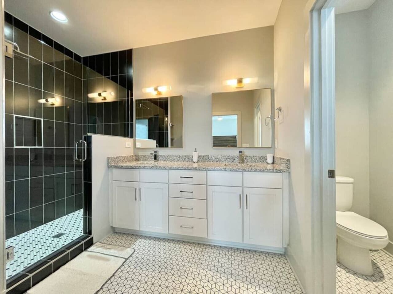Un baño moderno con cabina de ducha, inodoro y zona de lavamanos con espejo.
