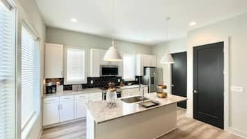 Una cocina moderna con armarios blancos, encimera de granito e iluminación colgante.