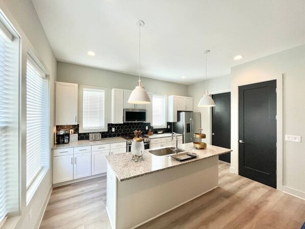 A modern kitchen with white cabinets, a granite countertop, and pendant lighting.