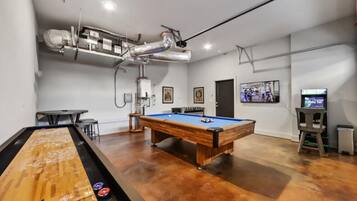 A billiards room with a pool table, a foosball table, and a television.