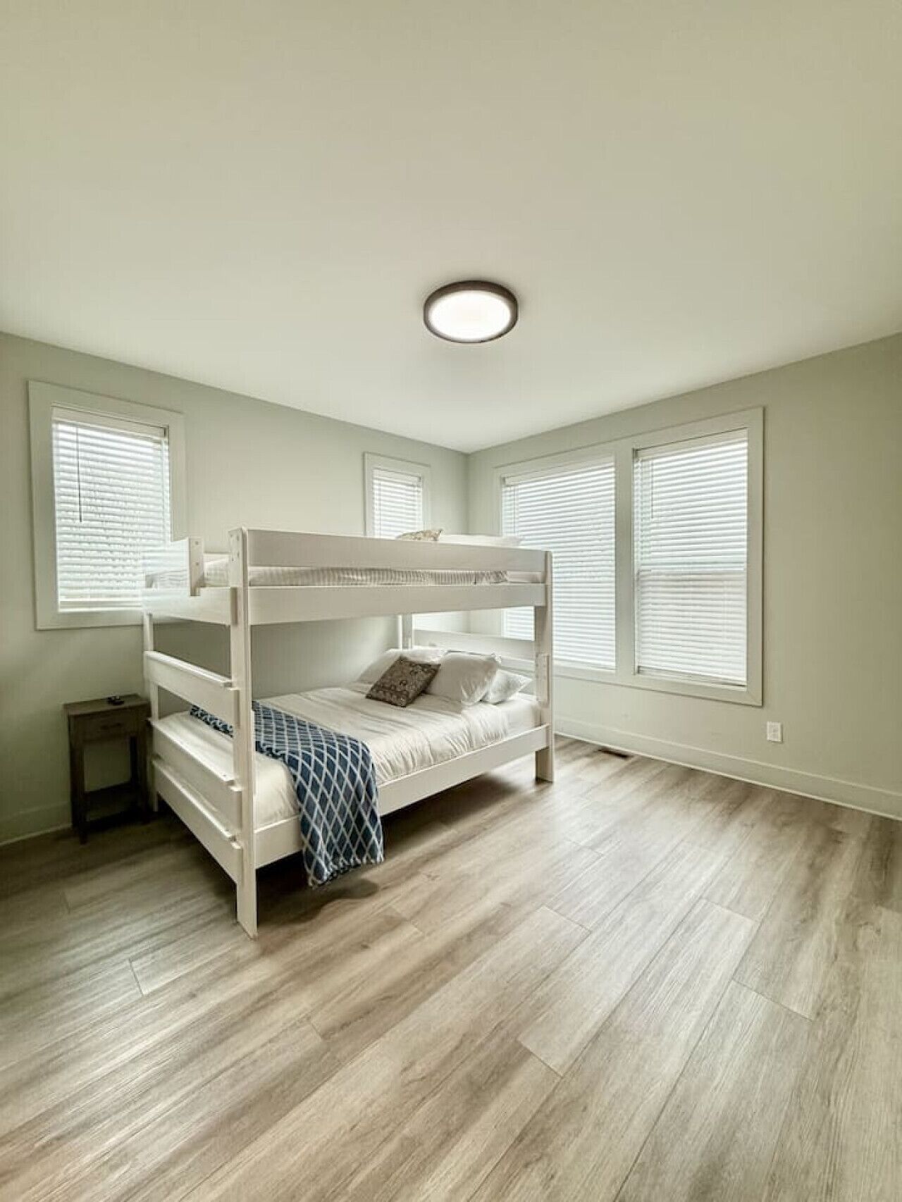 A room with a bunk bed, a small bedside table, and a window with blinds.