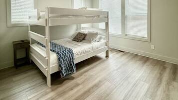 A room with a bunk bed, a small bedside table, and a window with blinds.