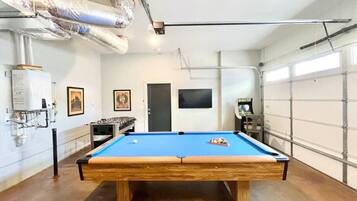 A pool table in a room with a garage door, a mounted TV, and a foosball table.