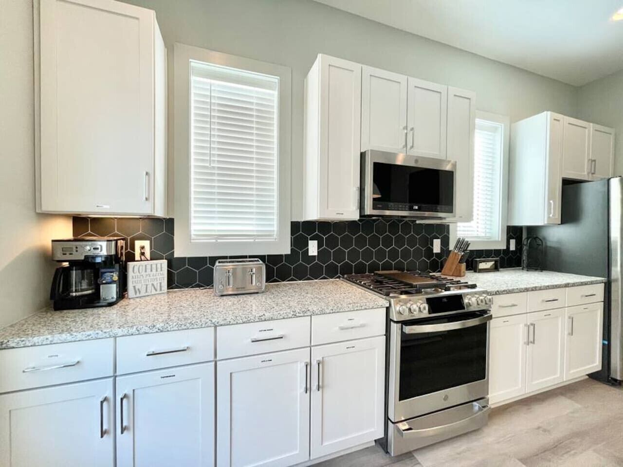 A modern kitchen with white cabinets, a stainless steel stove, and a microwave.