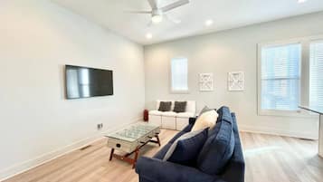 Una sala de estar moderna con un sofá azul oscuro, una mesa de centro de vidrio, un sofá blanco y un ventilador de techo.