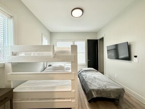 Ein Schlafzimmer mit Etagenbetten, einem Einzelbett, einem Fernseher und einer Tür zu einem anderen Raum.