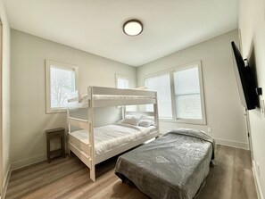 A bedroom with a bunk bed, a single bed, a small table, and a TV mounted on the wall.