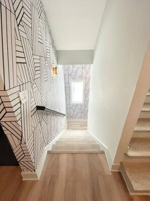 A staircase with geometric patterned walls and wooden flooring, leading to a room with a window.