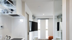 A modern kitchen with white cabinetry, a stainless steel kettle, and a flat-screen TV mounted above the counter. - Hotel SAILS Asakusa (Tokyo)