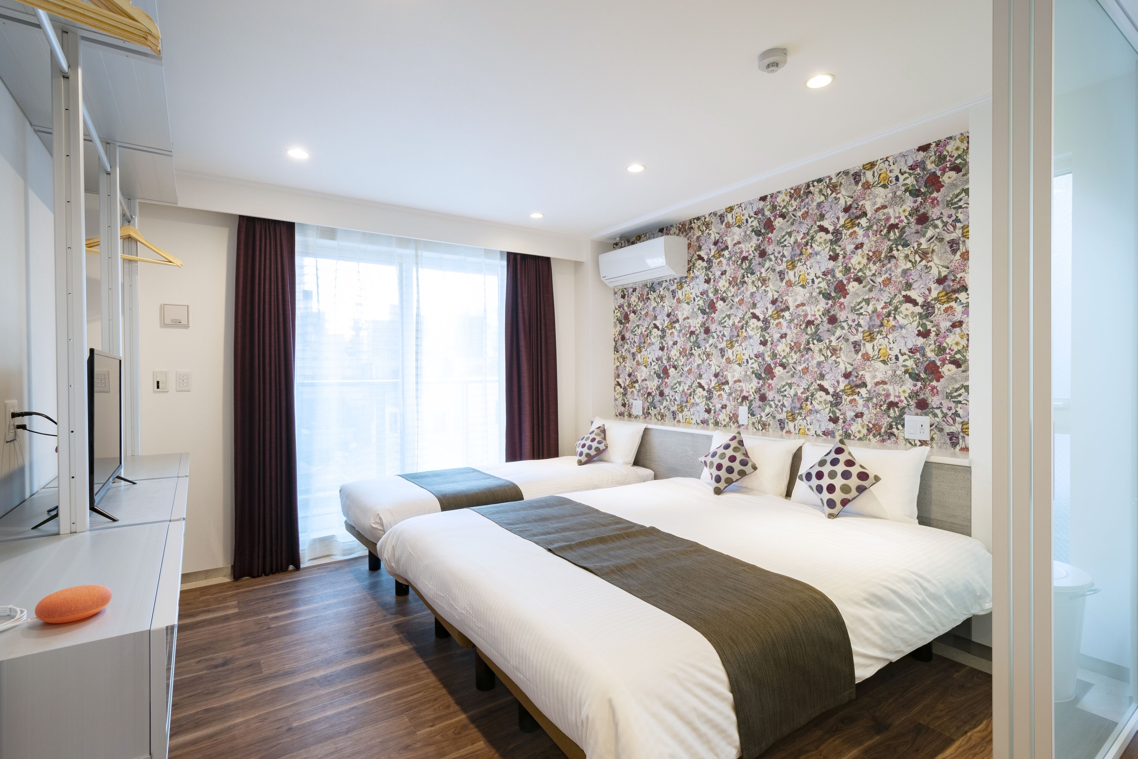 Una habitación de hotel moderna con dos camas, un ventanal grande y un papel tapiz con estampado floral.
