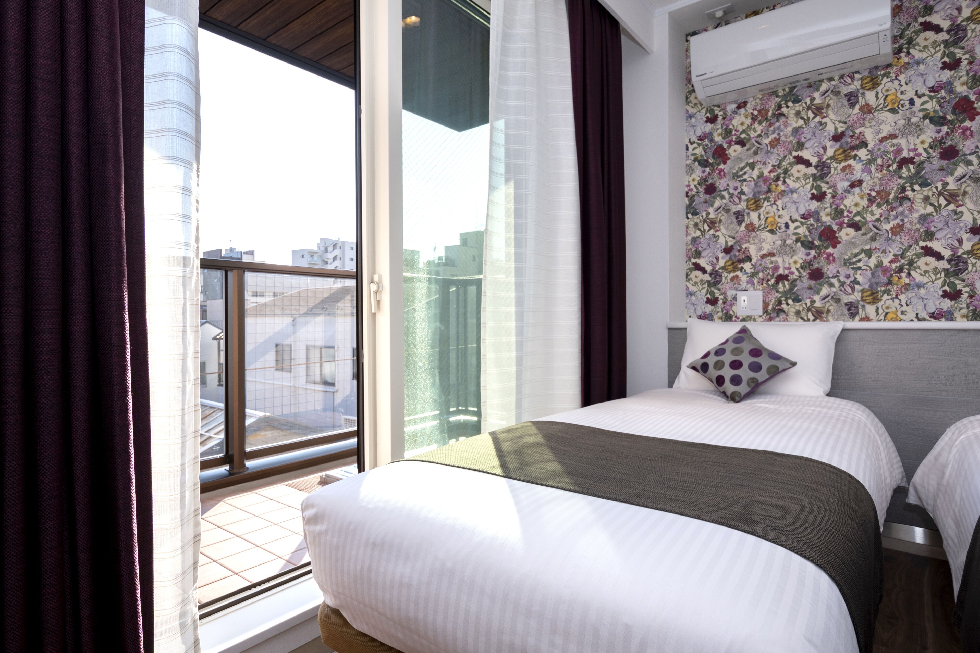 Ein Hotelzimmer mit einem großen Bett, Blick durch eine Schiebetür und floralem Wandpapier.