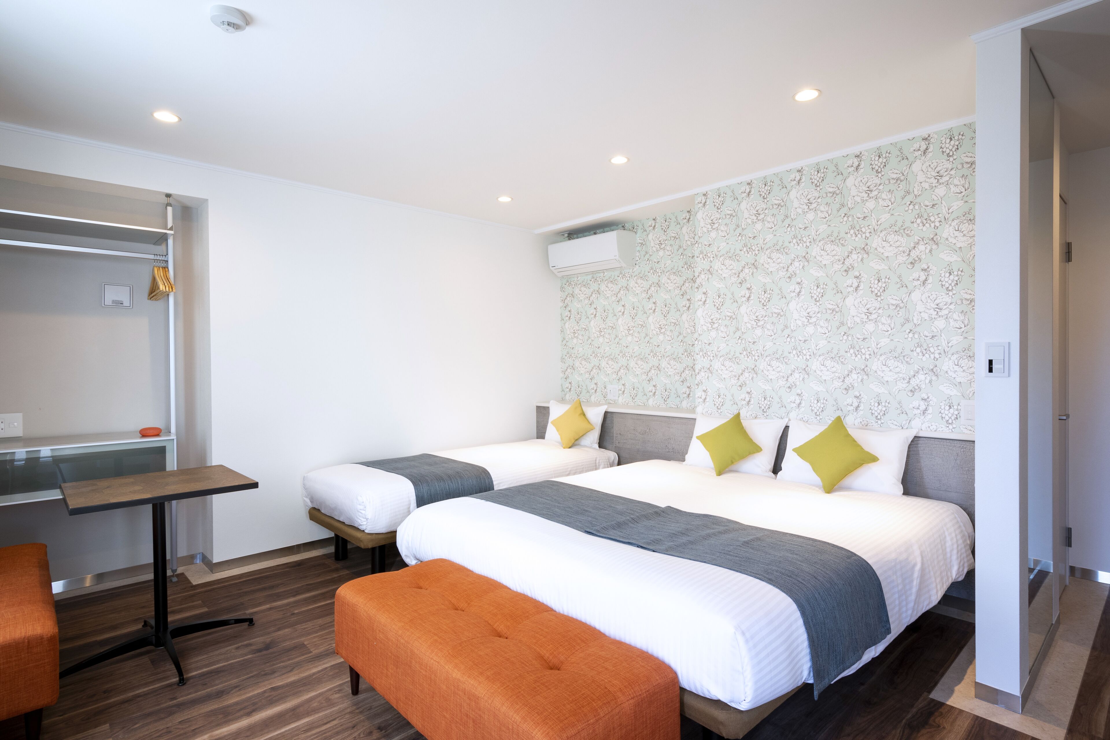 A hotel room with two beds, a desk, and an orange bench.