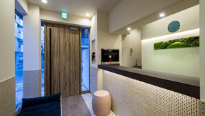 A modern reception area with a wooden door, a reception desk, a clock, and a green wall decoration. - Hotel SAILS Asakusa (Tokyo)