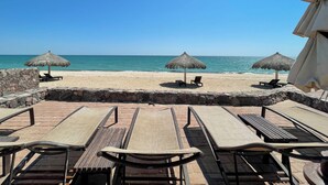 A beachside patio with lounge chairs and thatched umbrellas, overlooking the sea.