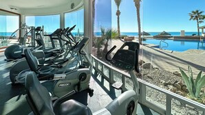 A gym with treadmills and exercise equipment, overlooking a pool and palm trees.