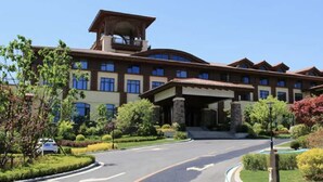 A large, multi-story hotel with a prominent entrance, landscaped gardens, and a clear sky.