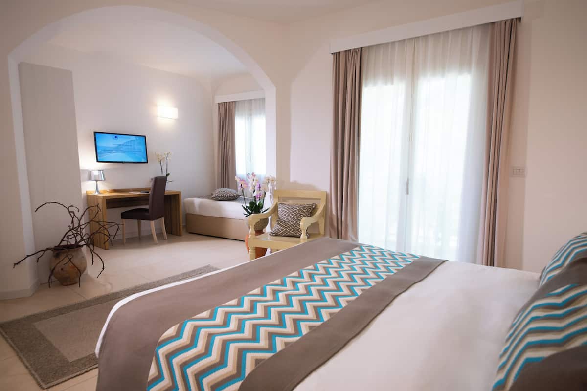 A hotel room with a large bed, a desk, a chair, and a television.