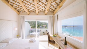Habitación de hotel con cama, un escritorio de madera, vista al mar y balcón con mobiliario exterior.