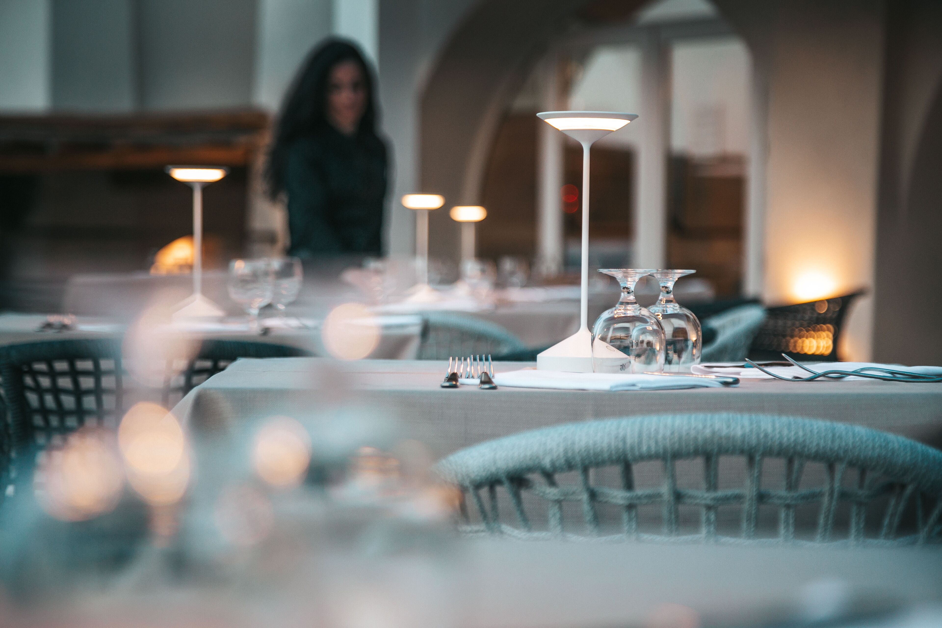 A restaurant setting with tables set for dining, featuring clear glassware and candle holders.