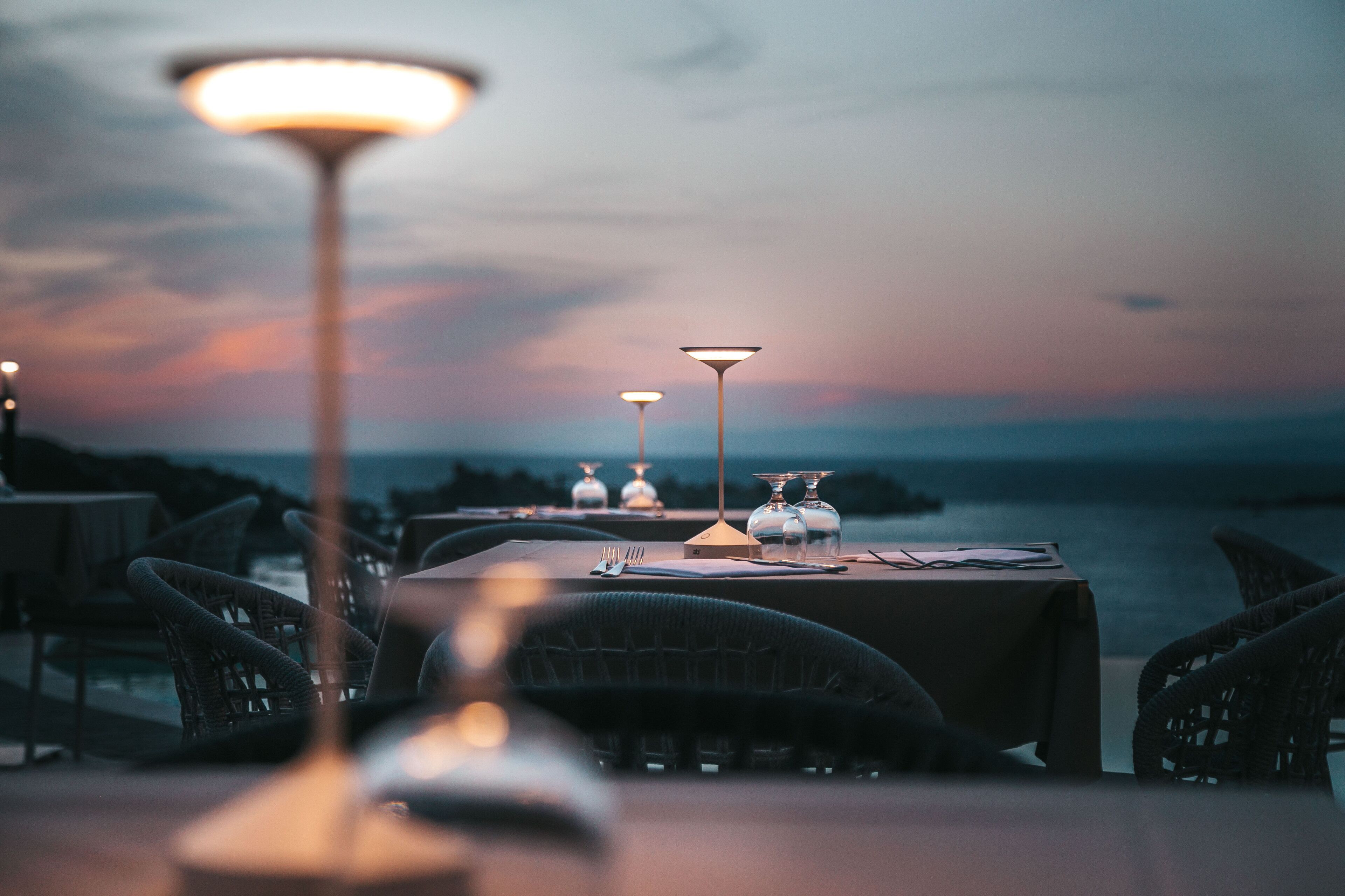 A restaurant setting with tables and chairs, a view of the sea, and decorative glass vases.