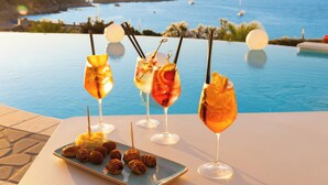 Una mesa con cuatro bebidas y un plato de pasteles junto a una piscina con vista al mar.
