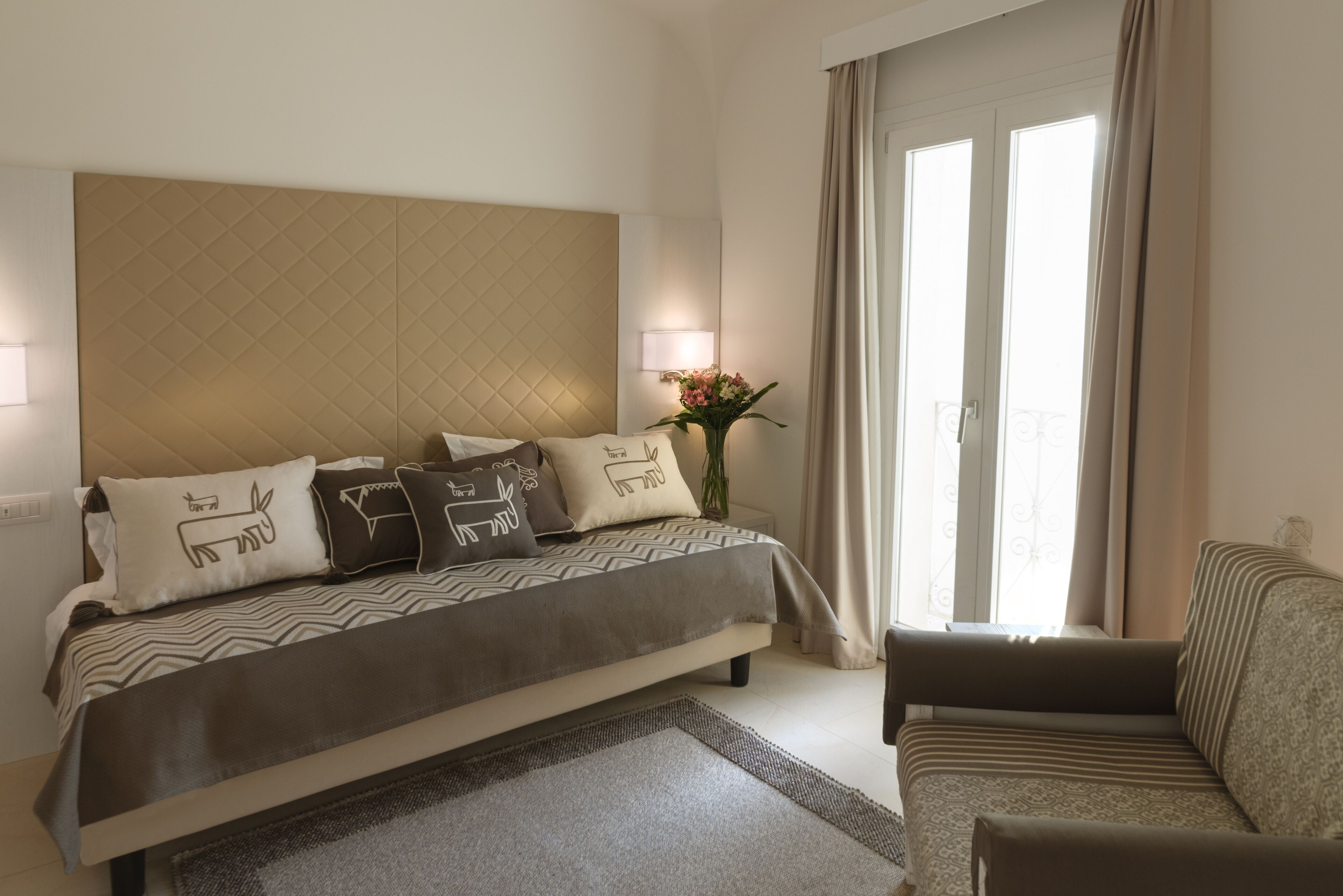 A bedroom with a bed, a sofa, a nightstand, a lamp, and a window with curtains.