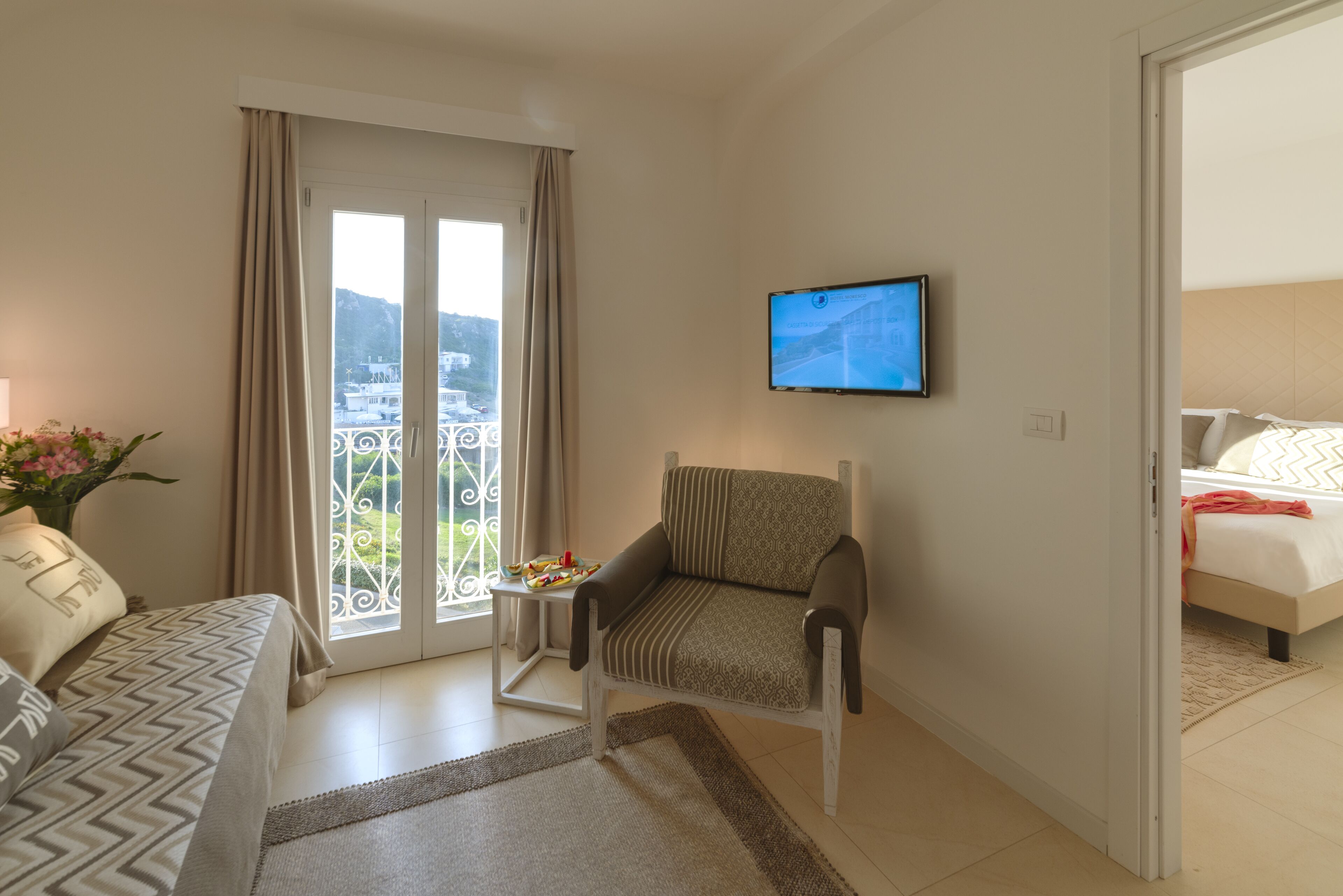 A hotel room with a bed, a sofa, a chair, a TV, and a balcony with a view.