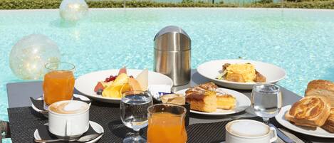 A breakfast setup by a pool with a clear view of the ocean.
