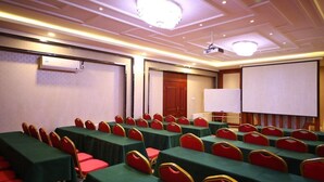 Une salle de conférence avec des rangées de tables et de chaises, un écran de projection et un tableau blanc.