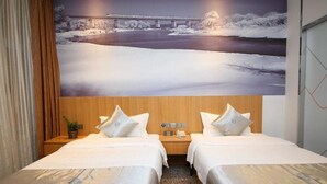 Une chambre d’hôtel avec deux lits, une grande image représentant un paysage enneigé accrochée au mur, une tête de lit en bois et une petite plante posée sur la table de chevet.