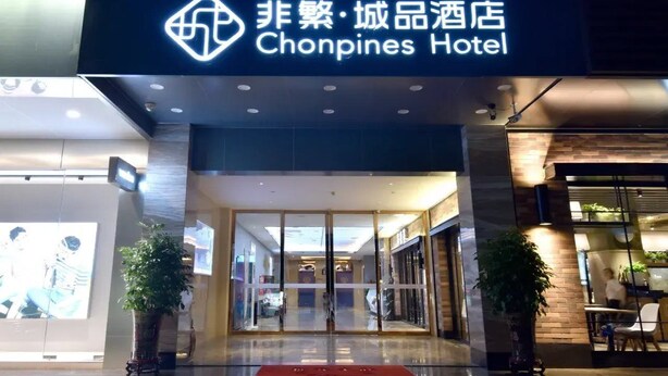 The exterior of the Chonpines Hotel with a modern design, featuring a glass entrance and potted plants. - Chonpines Hotel (Zhanjiang)