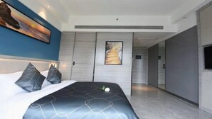 A modern hotel room with a large bed, a painting above the bed, and a view into the hallway. - Chonpines Hotel (Zhanjiang)